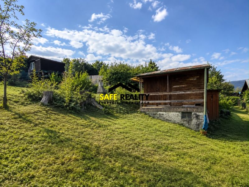 A wooden cottage in Žilina surrounded by green lawns and trees on a sunny day.