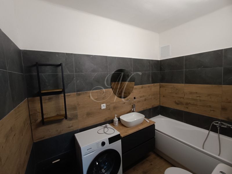 Bathroom in a 2-room apartment with wood-patterned flooring, a washing machine, and a bathtub.