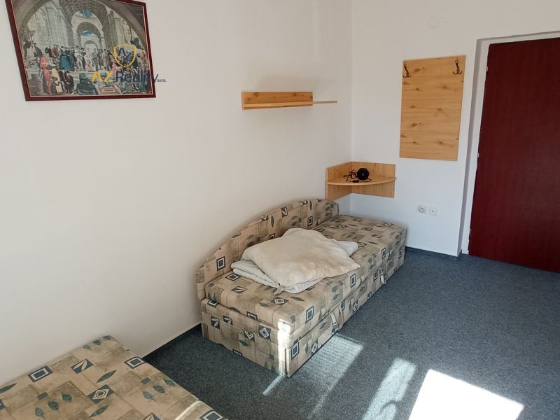 A hotel room with a sofa, a painting on the wall, a carpet, and wooden accessories.