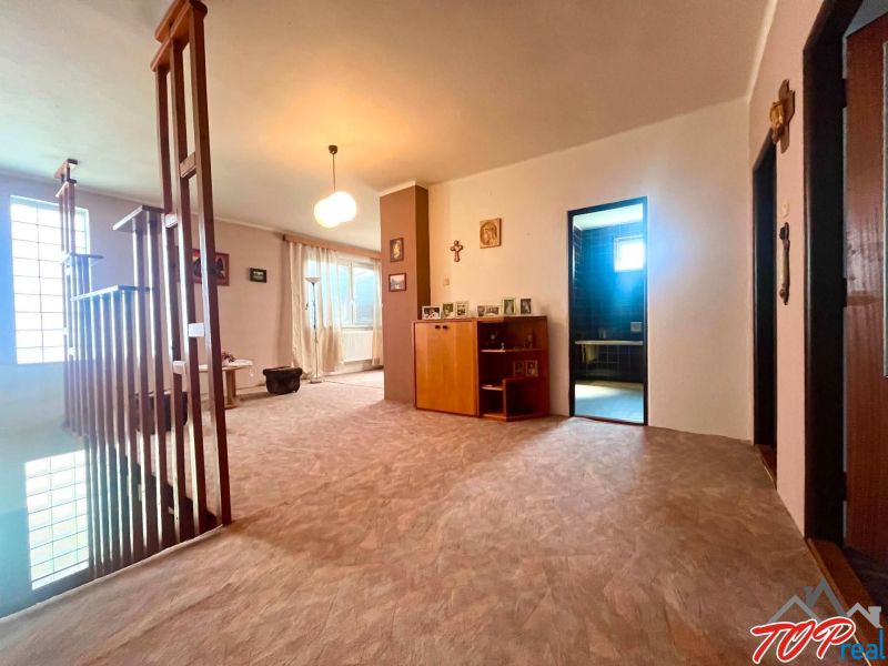 A hallway in a family house with wooden glass railings, decorations, and an entrance to the bathroom.