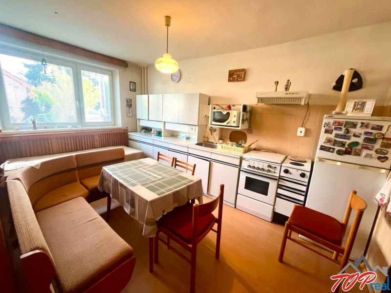 A kitchen with a dining area, an older stove, and a wooden-patterned floor in a family house.