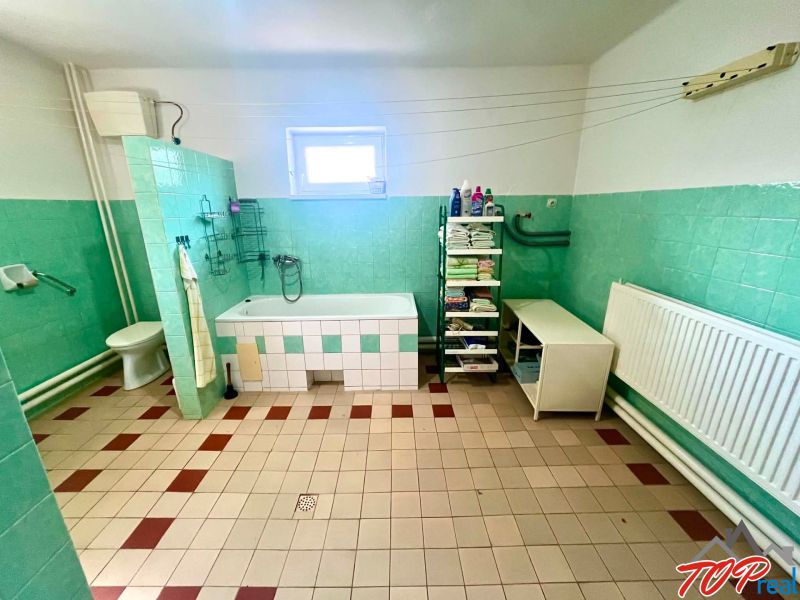 Bathroom in a family house with a bathtub, toilet, shelves, and a window.