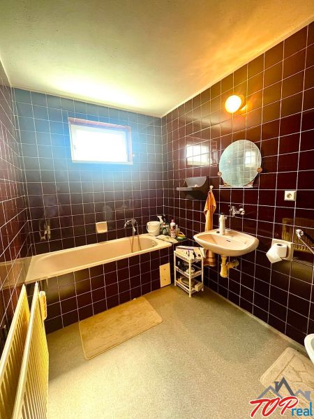 A bathroom in a family house with dark tiles, a bathtub, and a window on the wall.