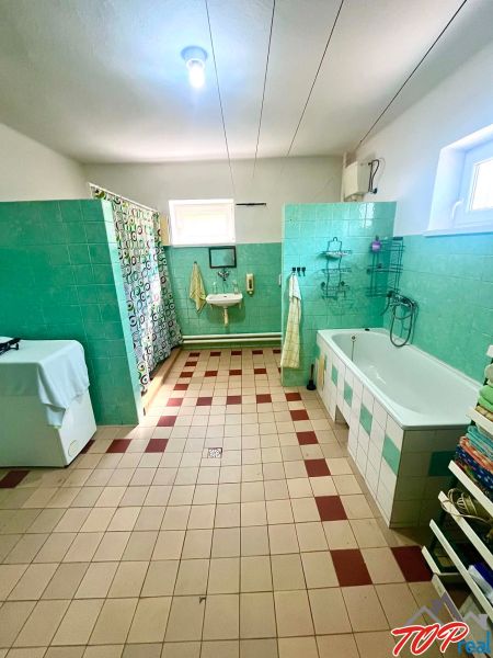 A bathroom in a family house with green tiles, a bathtub, and a washing machine.
