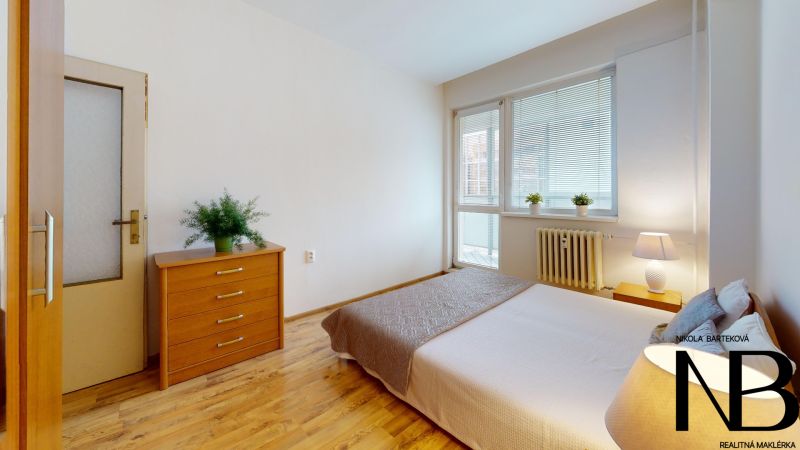 Cozy bedroom in a 2-room apartment on K výstavisku street with a wooden dresser and bed.