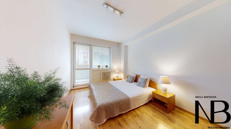 A bright bedroom with a large window and a bed in a 2-room apartment on K výstavisku street.