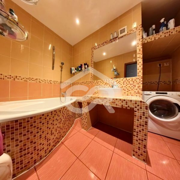 A bathroom in a 4-room apartment with orange tiles, a bathtub, and a washing machine.