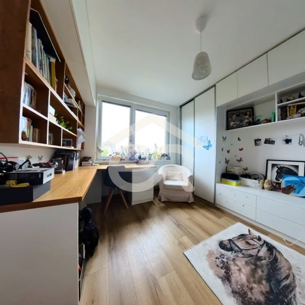 A study in a 4-room apartment with a wooden decor floor, shelves, and an armchair under the window.