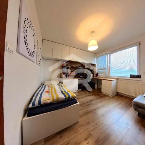 A room in a 4-room apartment with a wooden decor floor, a table, and a bed.
