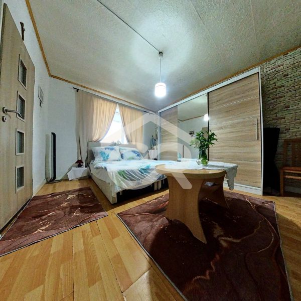 A bedroom in a family house with a wooden decor floor, flowers on the table, and a bed.