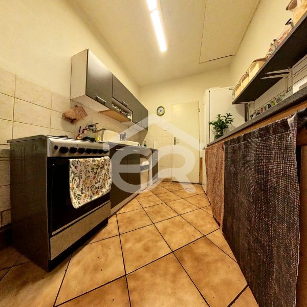 A narrow kitchen in a family house with ceramic tiles and a stainless steel stove.