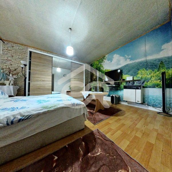 A bedroom in a family house with a bed, wall wallpaper, and a floor with a wooden decor.