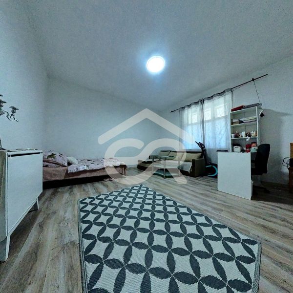 A room in a family house with a wooden decor floor, a bed, and a desk.