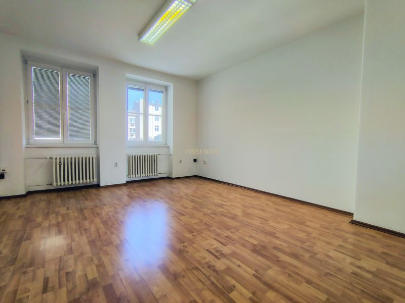 An empty office with wood-patterned flooring and large windows.