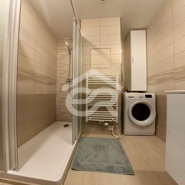 A bathroom with a shower and a washing machine in a 3-room apartment.
