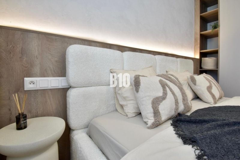 A bedroom with a headboard and shelves in a 4-room apartment, with soft lighting.