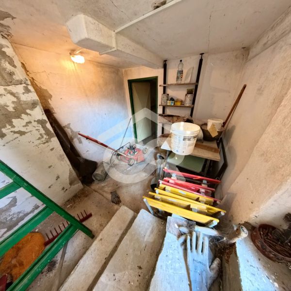 A shed with garden tools and a lawnmower, stored on stairs and shelves.