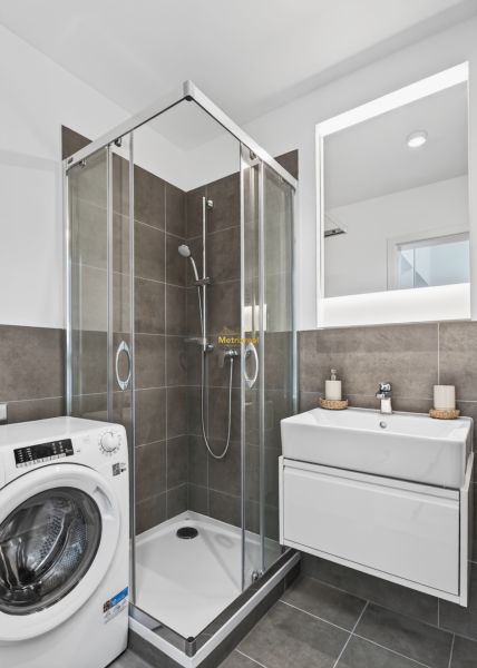 A bathroom in a studio apartment with a shower, a sink, and a washing machine.