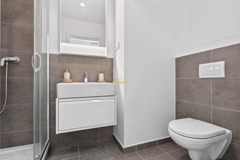 A bathroom in a studio apartment with a sink, shower, and toilet, tiled with tiles.