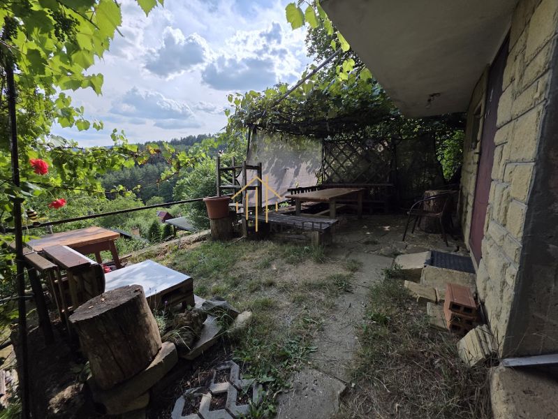A cottage in Banská Bystrica with rustic seating and vine, surrounded by nature.