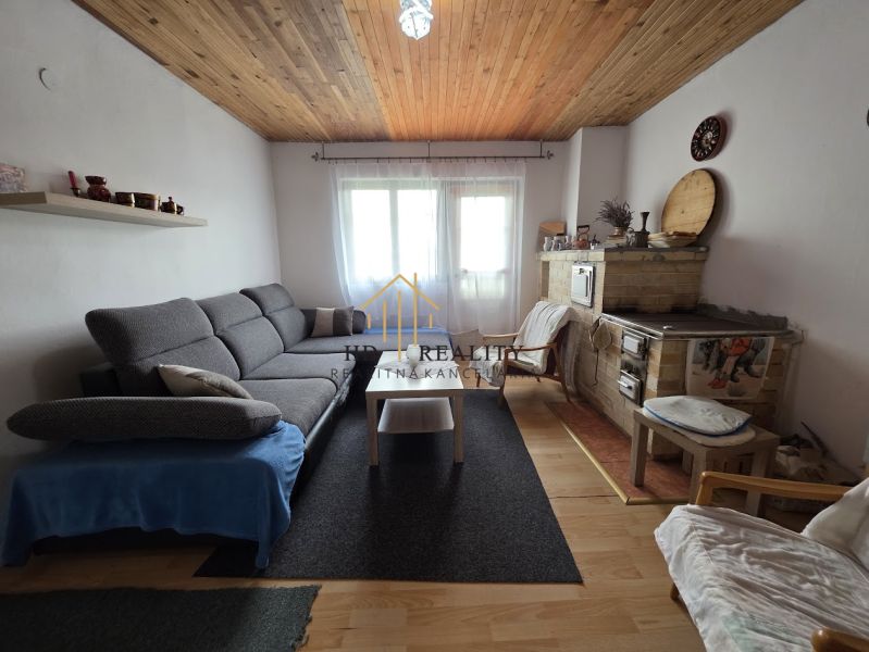A living room of a cottage with a comfortable sofa, a tiled stove, and a wooden-patterned floor.