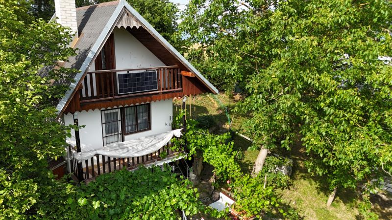 A cottage in Banská Bystrica surrounded by greenery with a wooden balcony and a photovoltaic panel.