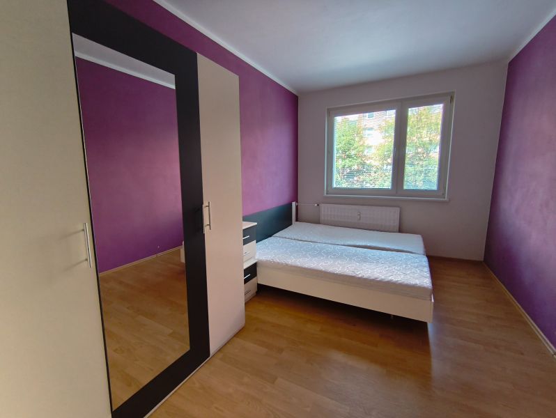 A bedroom in a three-room apartment with a wooden decor floor and purple walls.
