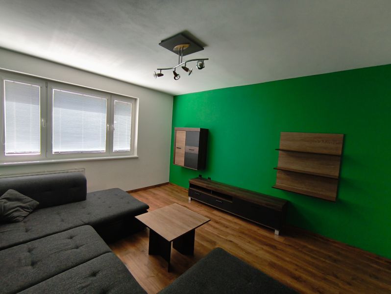 Living room in a 3-room apartment with a wooden decor floor and a green wall.