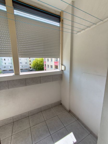 A balcony with ceramic tiles, a drying rack, and a view of the surrounding buildings in a 3-room apartment.