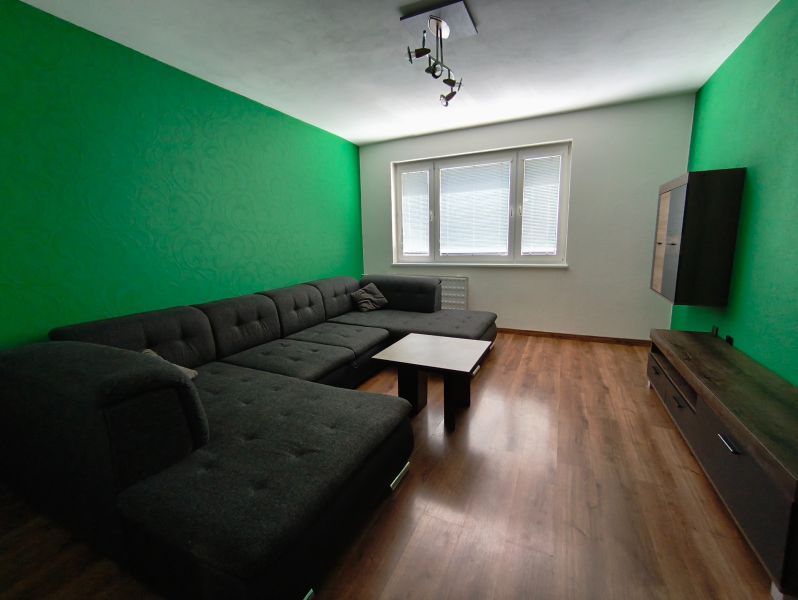 Living room with a dark couch, green wall, and wood-patterned floor.