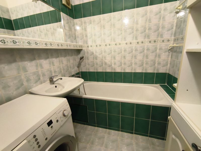 A bathroom with green and white tiles, a bathtub, and a washing machine, a 3-room apartment.