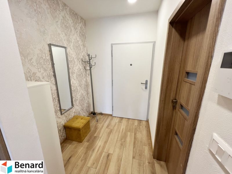 Entrance hall in a 1-room apartment with wallpaper, mirror, and wooden decor flooring.
