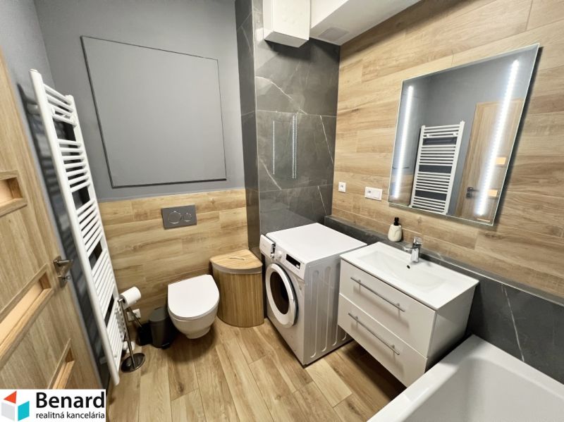 A bathroom in a studio apartment with a wood-patterned floor, a sink, and a washing machine.