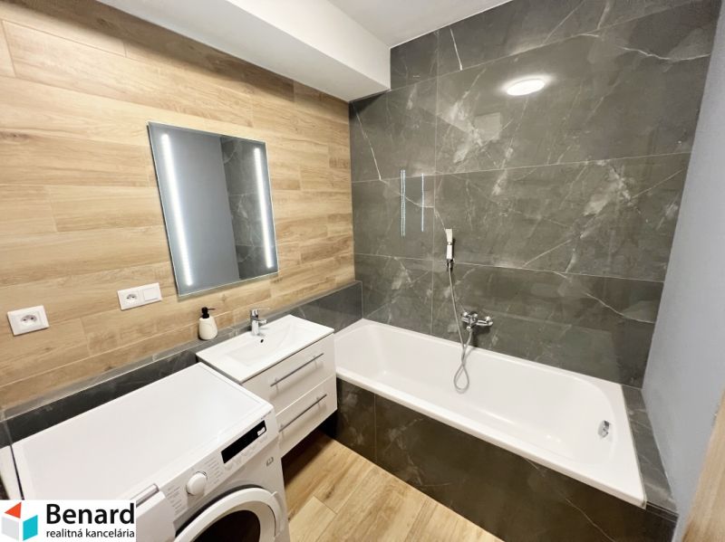 Bathroom in a studio apartment with a bathtub, sink, and washing machine, floor with wood decor.