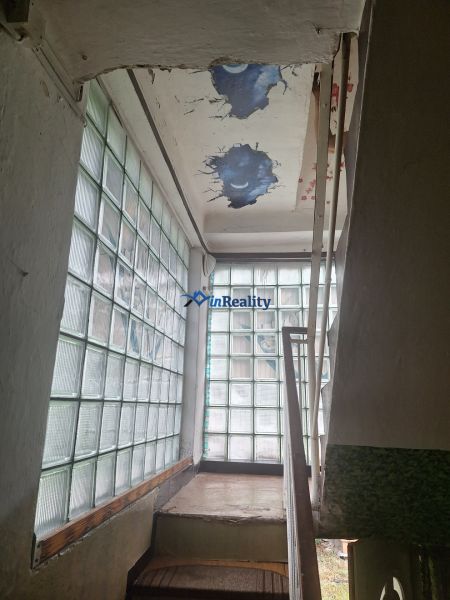 A staircase in a family house with a glass wall and a damaged ceiling.