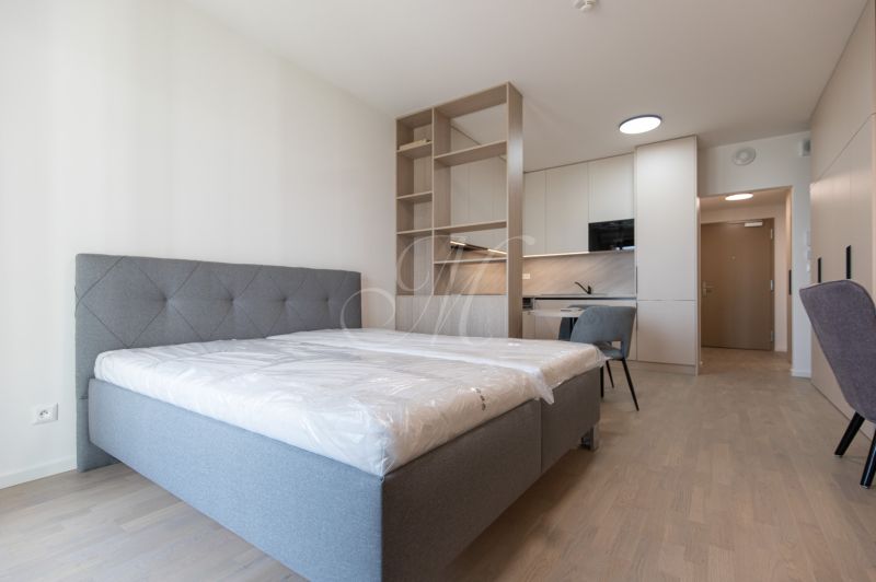 A one-bedroom apartment's bedroom with a bed, kitchenette, and wooden decor flooring.
