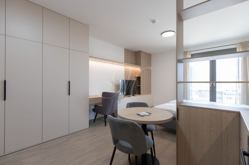 1-room apartment with wood-patterned flooring, wardrobes, a table, chairs, and a window.
