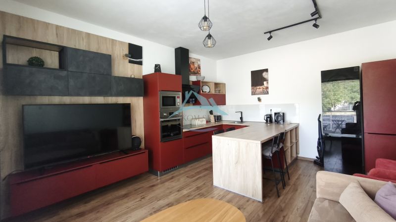 Living room in a two-room apartment with a red kitchen unit and a wooden decor floor.