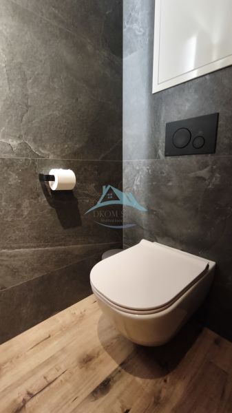 A bathroom with a wall-mounted toilet and a floor with a wood decor in a 2-room apartment.