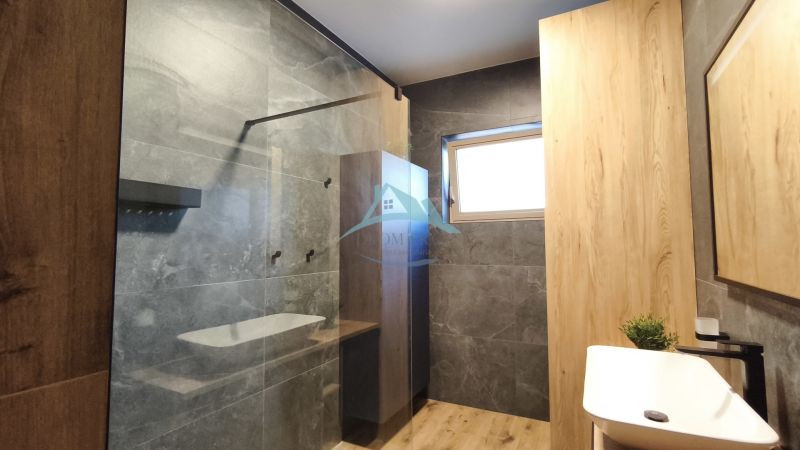 A bathroom with dark tiles, a shower corner, and a floor with a wooden decor in a 2-room apartment.