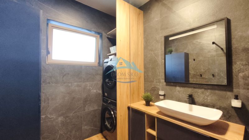A bathroom in a 2-room apartment with dark tiles and a washer with a dryer.