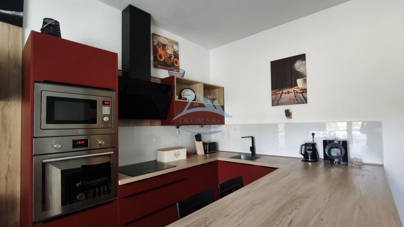 A kitchen with red cabinets and appliances in a 2-room apartment with a wood-patterned floor.