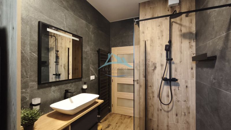 A bathroom with a wooden decor floor, a shower, and black details in a 2-room apartment.