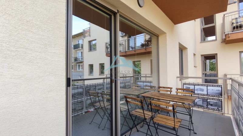 A balcony with seating in a 2-room apartment with a view of neighboring buildings.