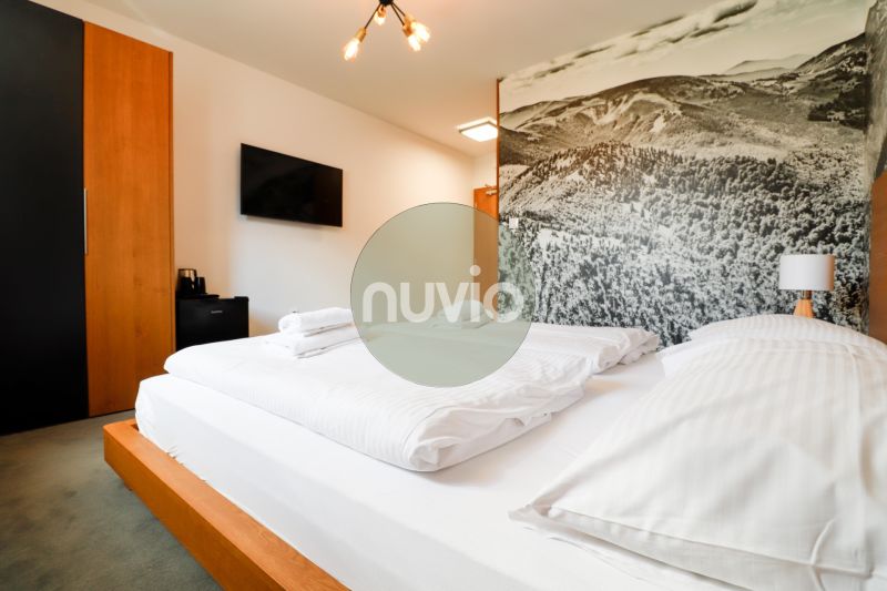 Bedroom of a vacation apartment with a large bed, a picture of mountains, and a TV on the wall.
