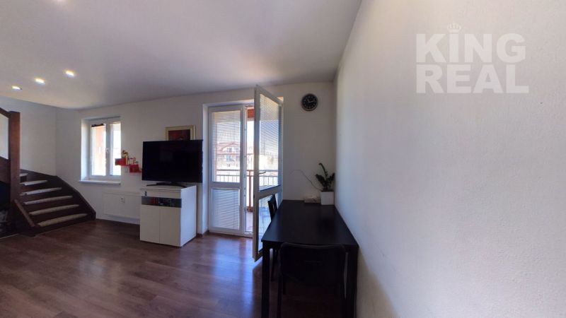A room of a 2-room apartment with a wooden decor floor, a table, and a television.