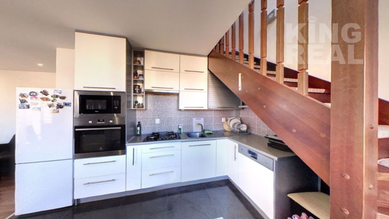 A kitchen in a 2-room apartment with stairs and appliances, with a wooden decor floor.