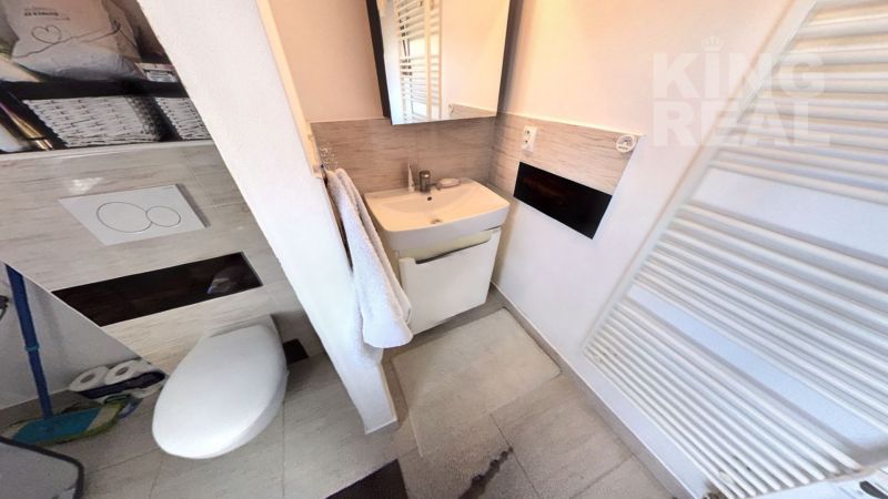 Bathroom in a 2-room apartment with a sink, mirror, and wall-hung toilet.