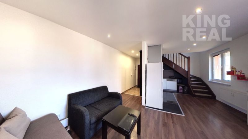 Living room of a 2-room apartment with a sofa, a table, and a staircase. Floor with wood decor.