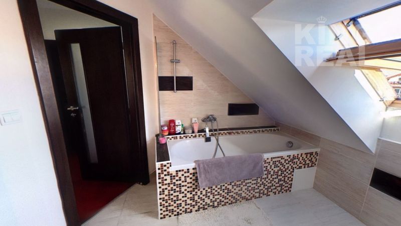 Bathroom with a bathtub in the attic of a 2-room apartment, light tiles, sloped roof.